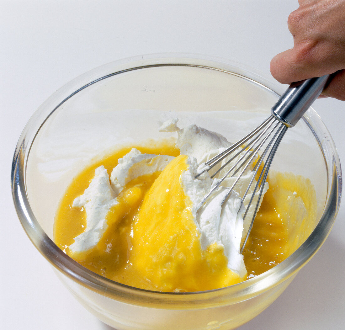 Close-up of hand whisking mango puree and whipped cream