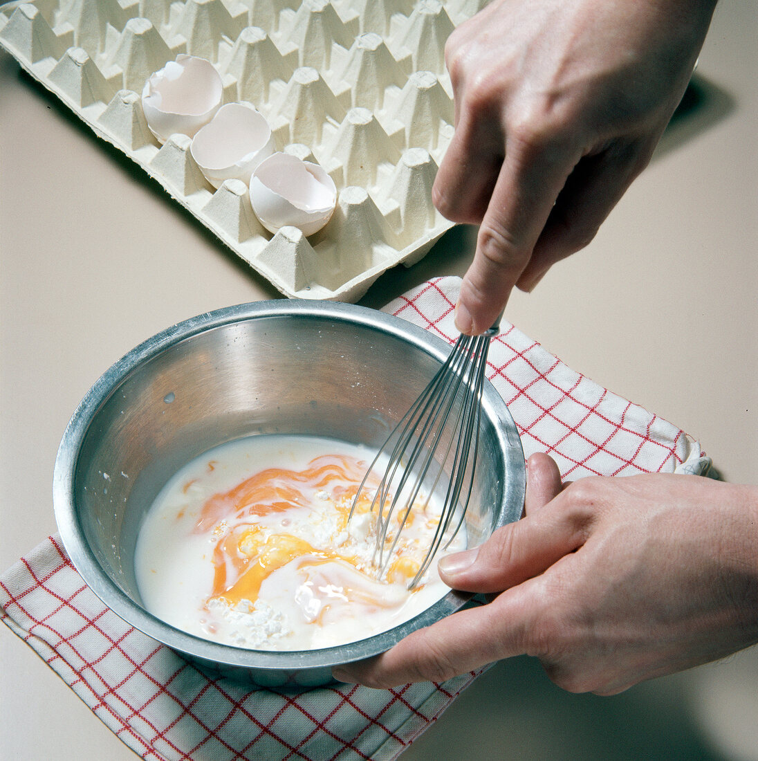 Close-up of hand whisking eggs, flour and milk in pot for preparation of dessert, step 2
