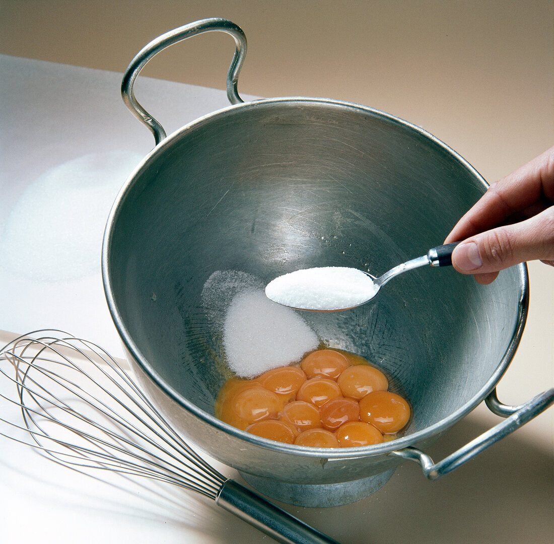 Sugar being added in wok with egg yolks for preparation of biscuits, step 1