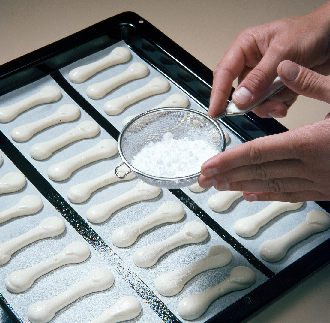 Close-up of hand sprinkling icing sugar with sieve on biscuits, step 8