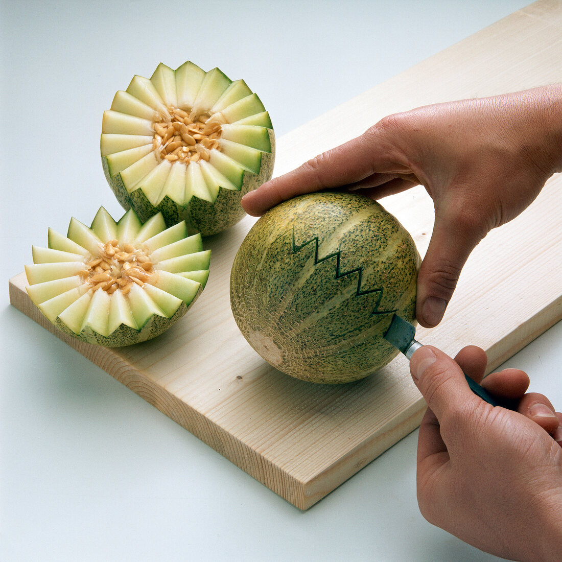 Close-up of hand cutting melon in jagged shape on white background
