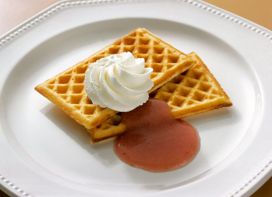 Waffles with strawberry sauce and whipped cream on plate