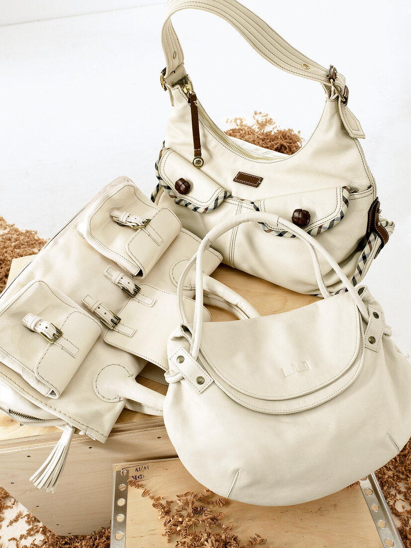 Three white handbags lying on wooden crates between wood chips