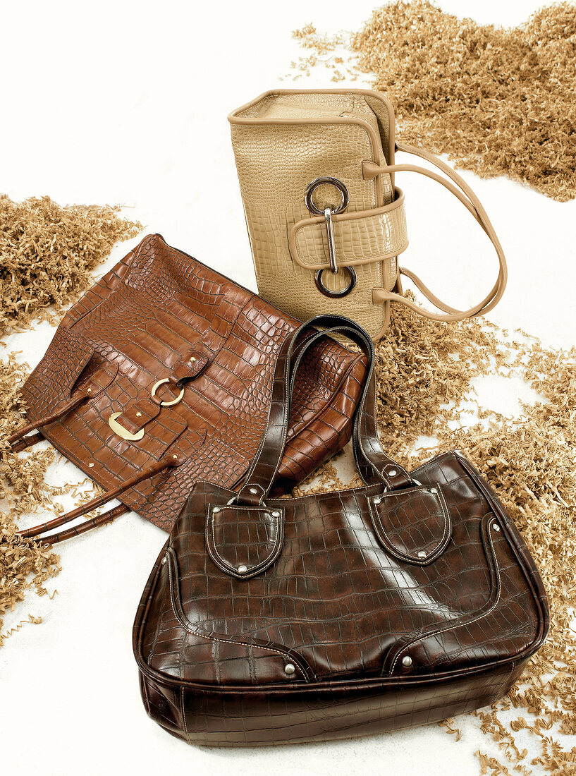 Three handbags in brown and beige between wood chips