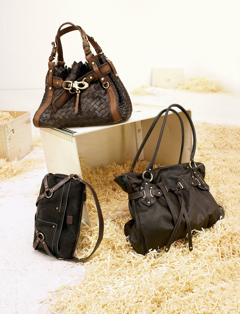 Three handbags in brown and black between wood chips