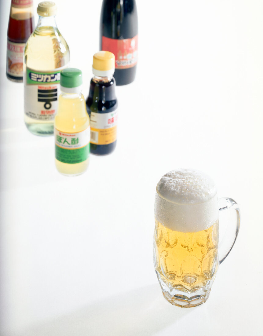 Glass of rice beer and vinegar bottles on white background