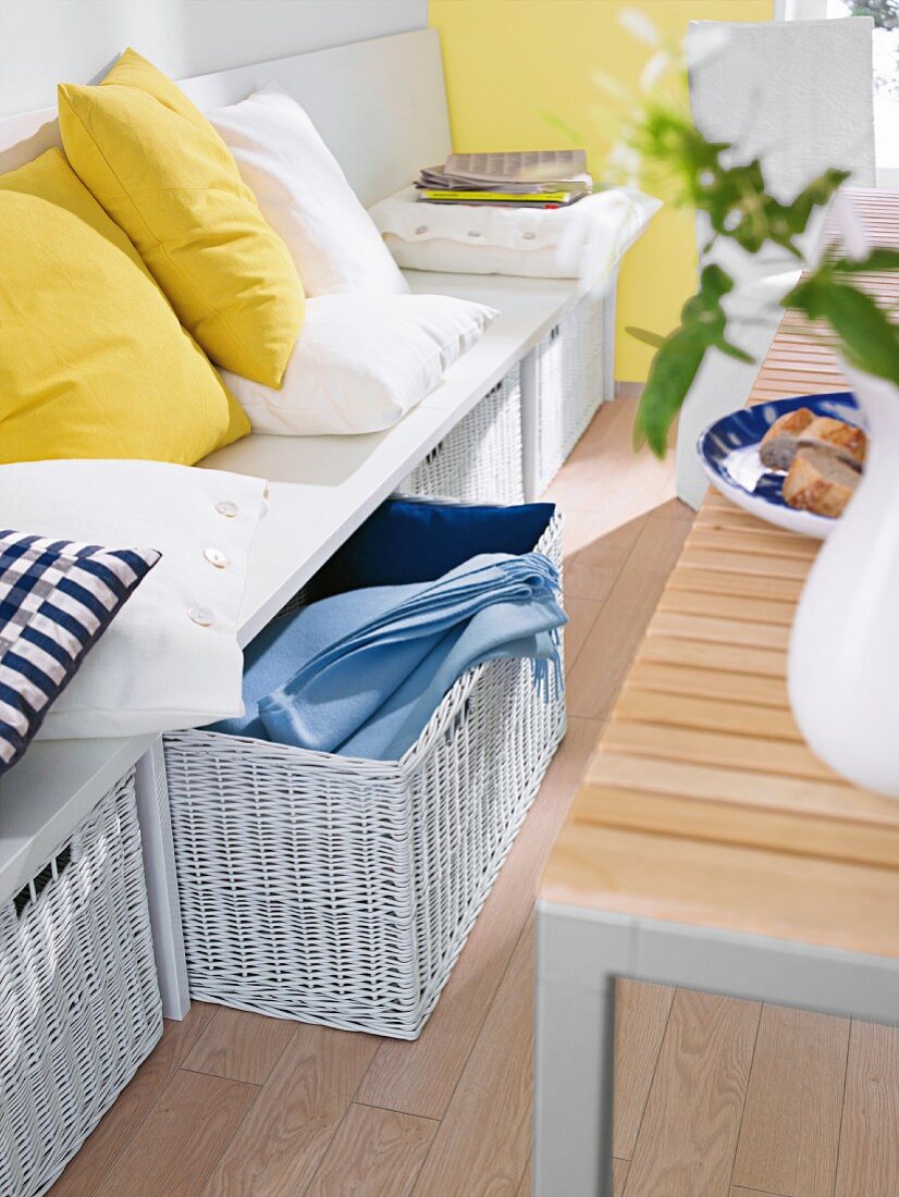 Storage baskets below white bench with scatter cushions