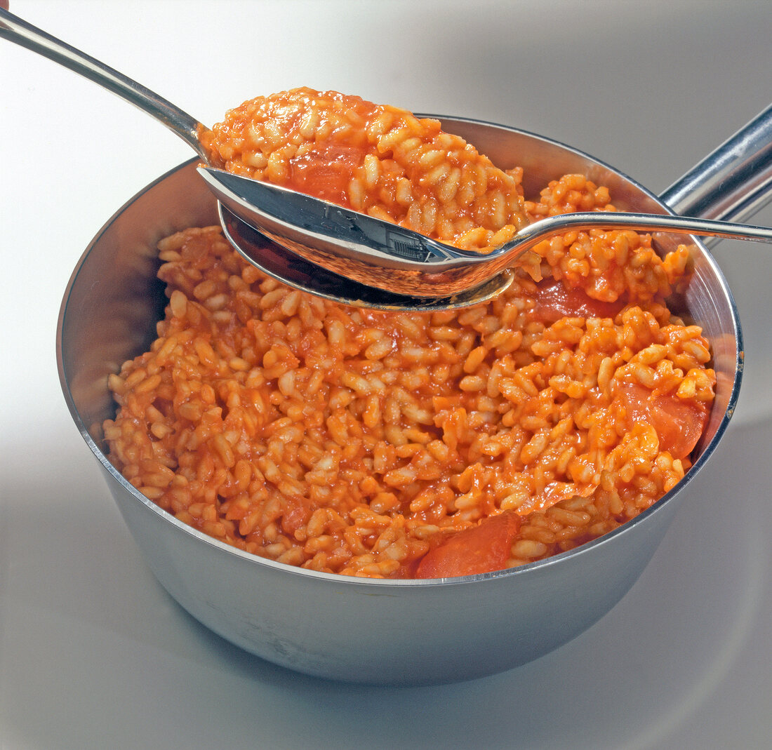 Close-up of hand mixing tomato rice with spoon in saucepan, step 2