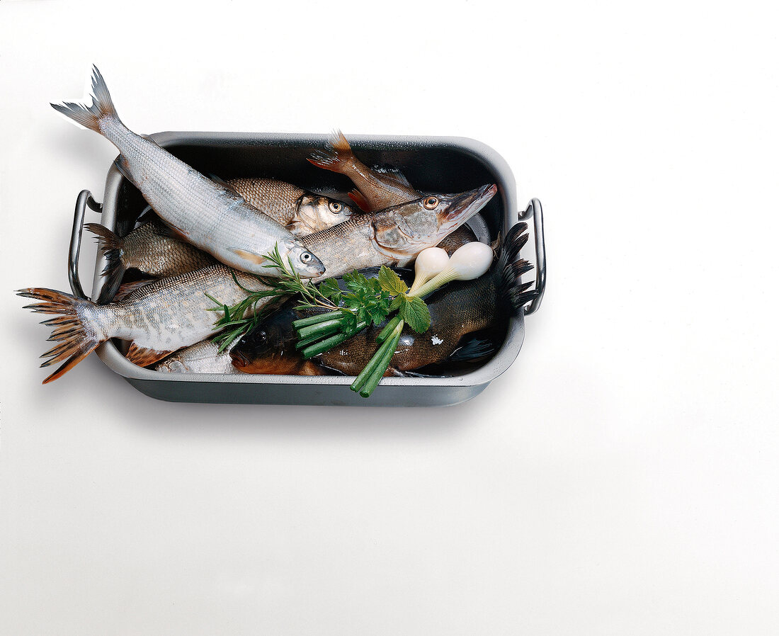 Raw fish and vegetables in roasting dish on white background