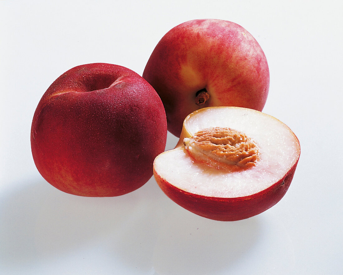 Whole and halved peaches on white background