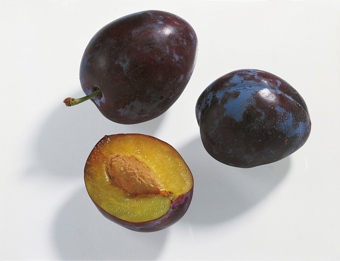 Whole and halved plums on white background