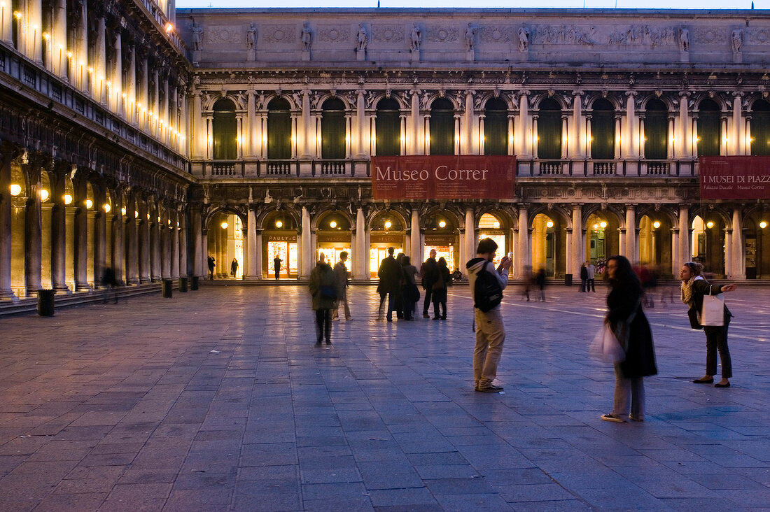 Tourist in front of illuminated arcades at Saint Mark's Square in evening, Venice, Italy