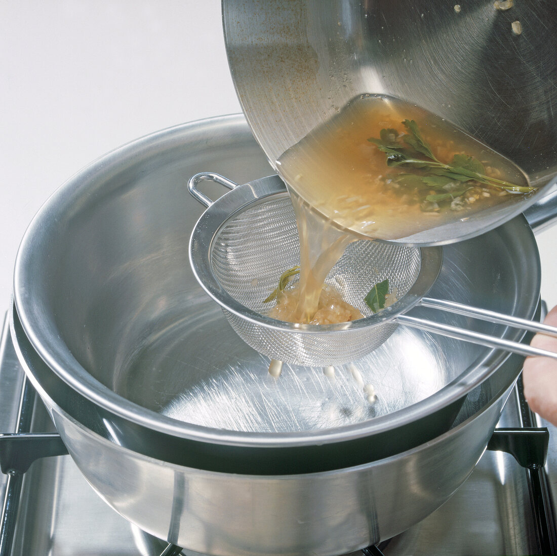 White wine with herbs being poured in bowl through sieve, step 5