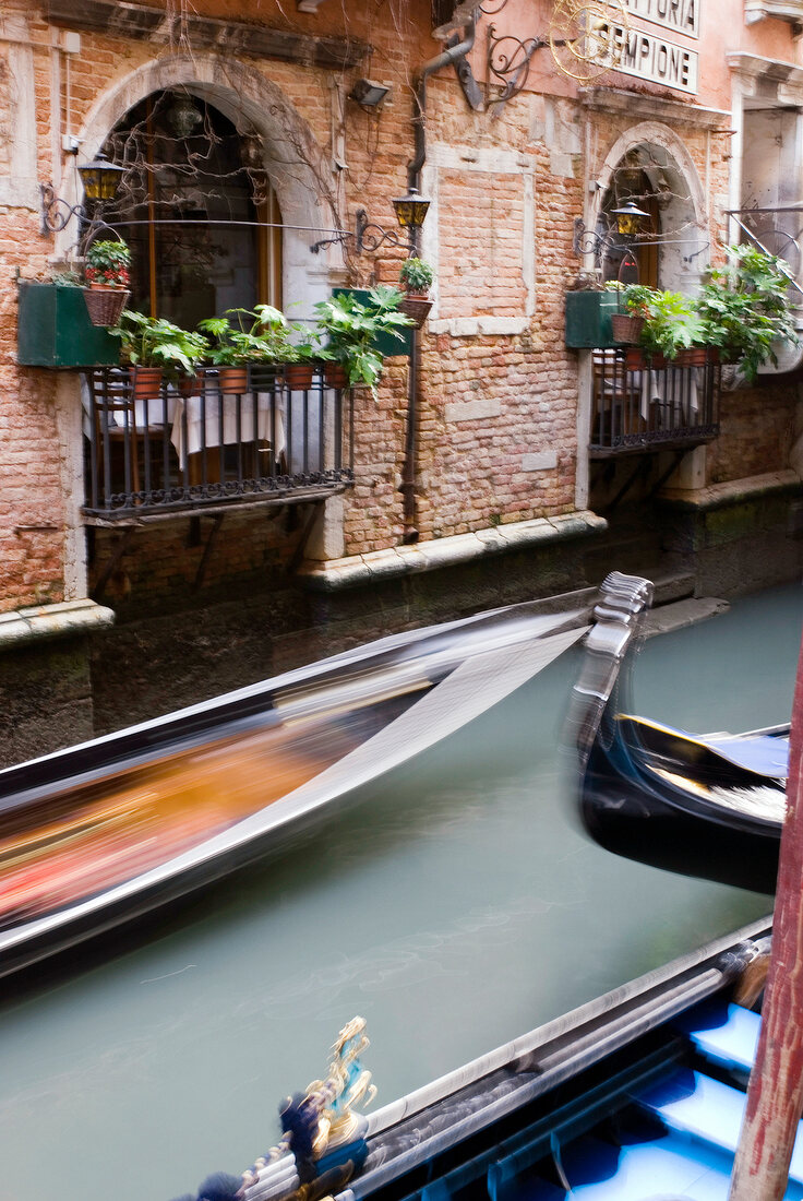 Gondolas speeding in narrow canal beside balcony, Venice, Italy, blurred motion