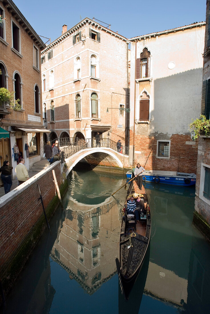 Tourists enjoying gondola ride in narrow canal with buildings on side, Venice, Italy