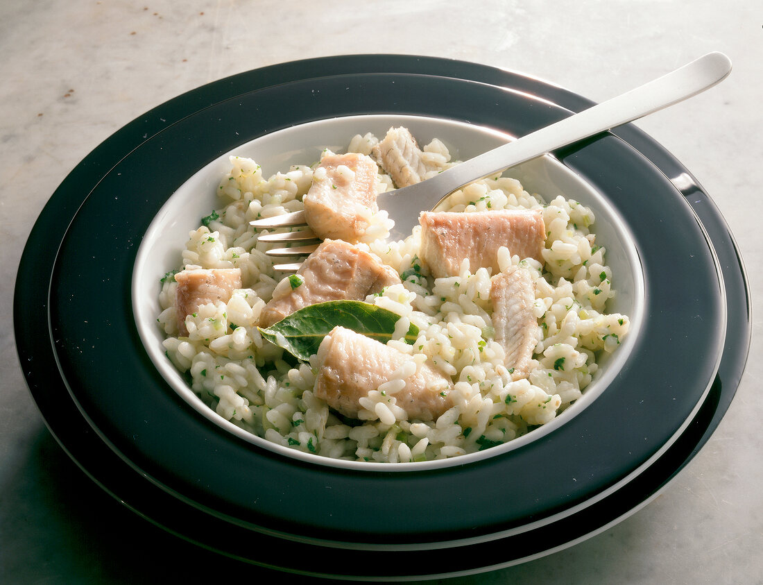Risotto with bay leaf and chopped parsley in bowl with fork