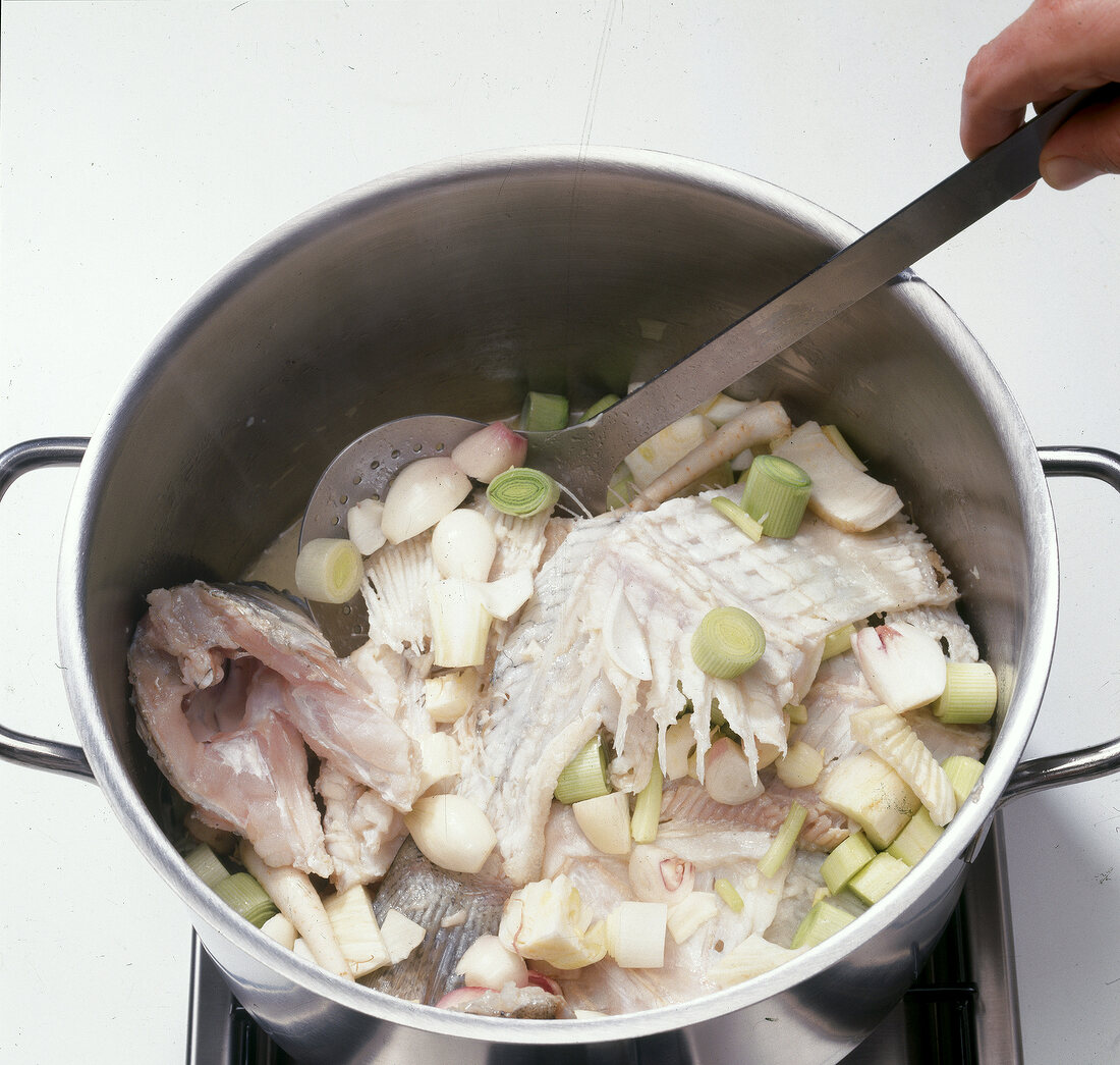 Close-up of vegetables with carcasses in casserole to prepare fish stock, step 3