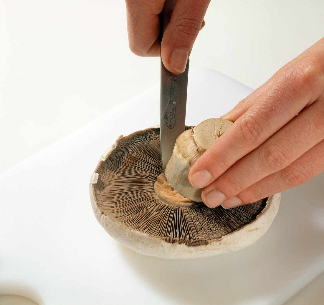 Close-up of hand cutting stem of portobello mushroom with knife, step 2