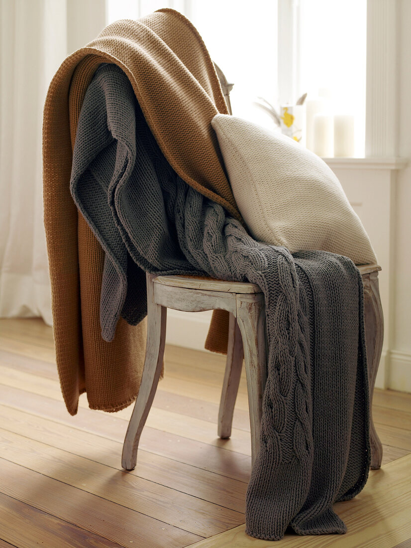 Kissen und Decken in Strick-Optik auf Stuhl, braun