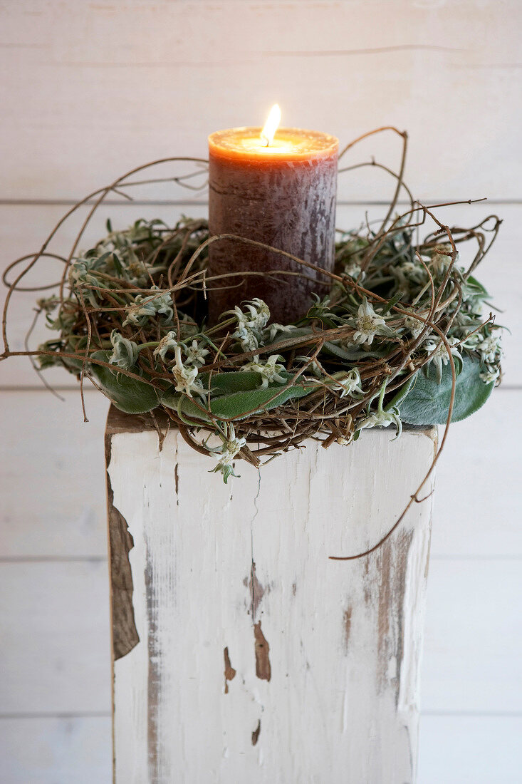 Lit candle in wreath of persicaria and edelweiss flowers