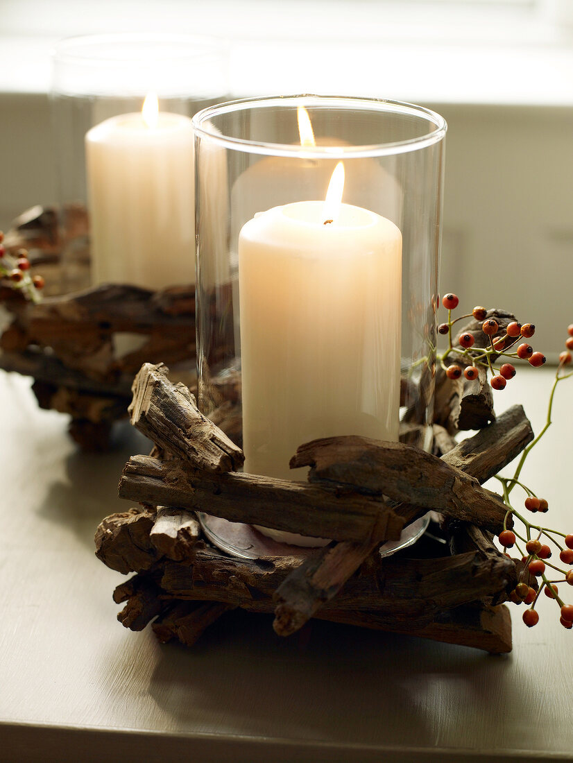 Lit candle in tall glass decorated with wood and berries