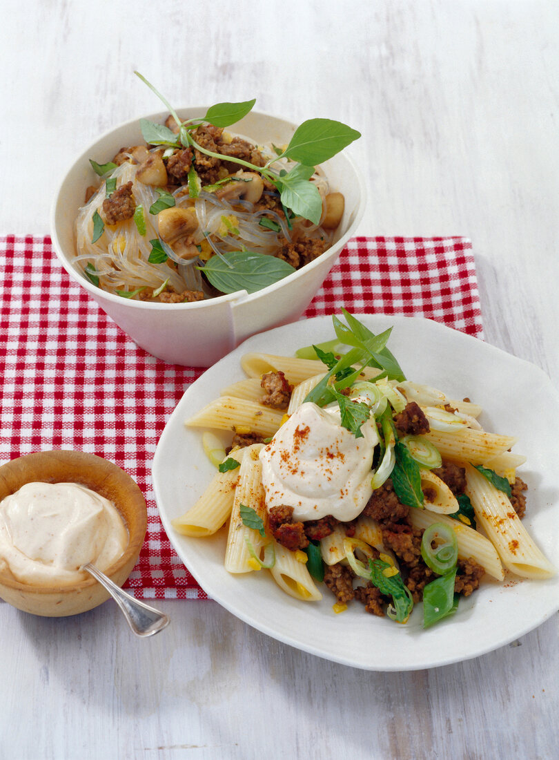 Rice noodles in bowl and penne with mince and yogurt on plate