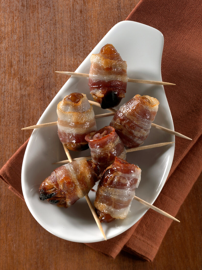 Skewered stuffed dates wrapped in bacon in serving dish