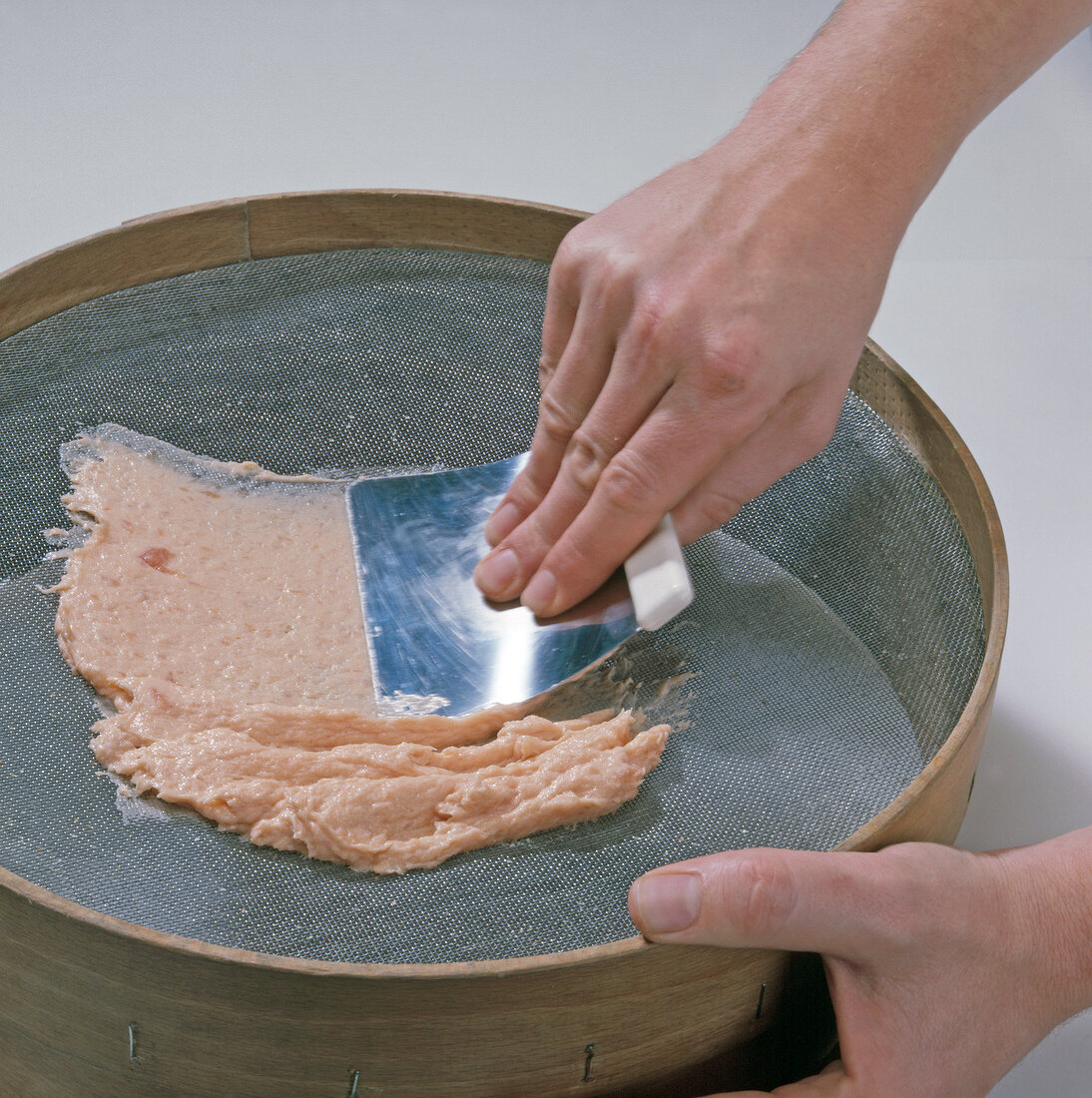 Close-up of hand spreading salmon through sieve, step 2