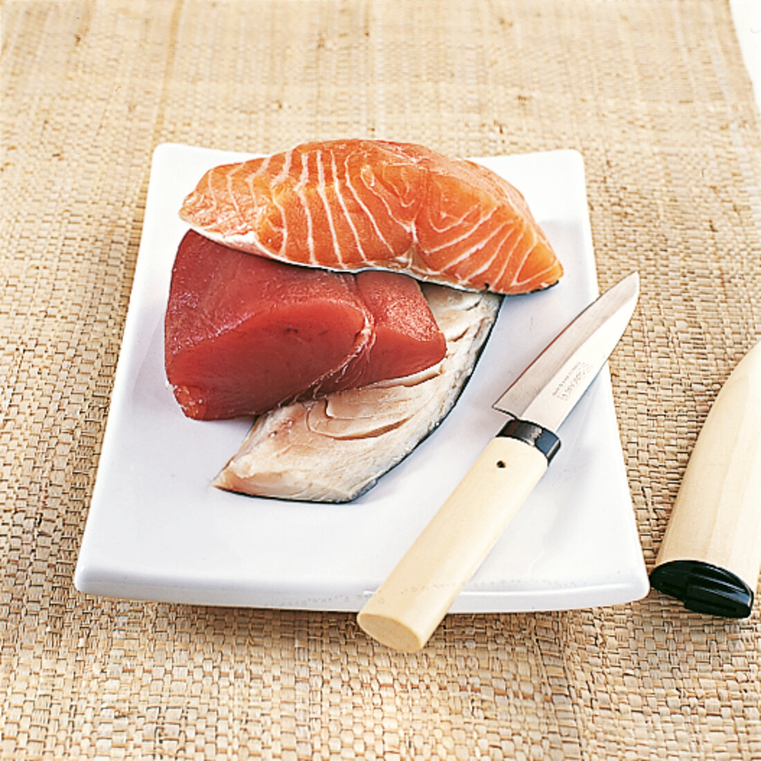Three species of raw fish on porcelain plate with knife