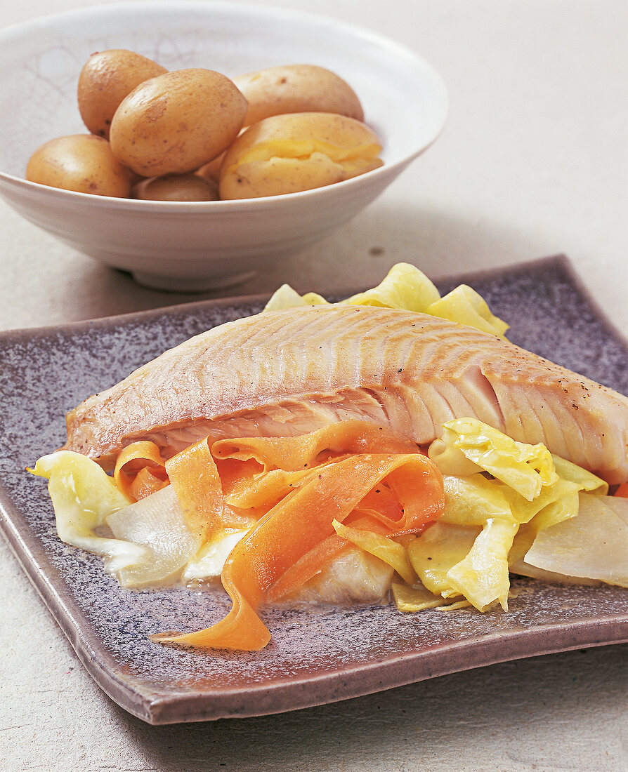 Tilapia fillets on spring vegetables on plate and boiled potatoes in bowl