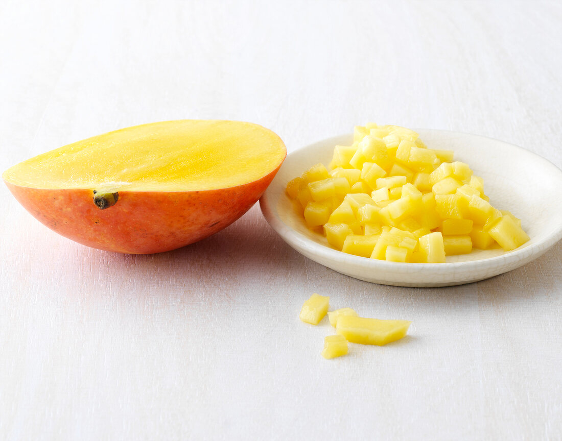 Mango cubes on plate beside halved mango