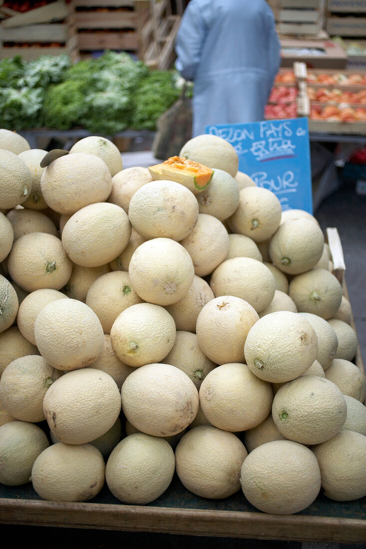 People buying cantaloupe charentais melons in wooden boxes at market