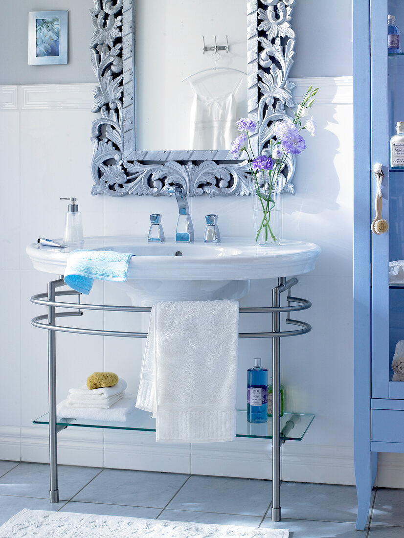 Weißes Waschbecken, verzierter Spie- gel, blauer Badezimmerschrank