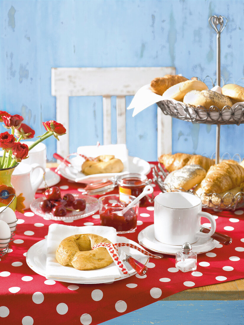 Breakfast table with red and white polka dot table cloth, rolls, croissants, jam and eggs