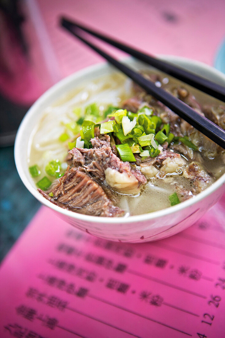 Soup with beef brisket, noodles and spring onions in bowl