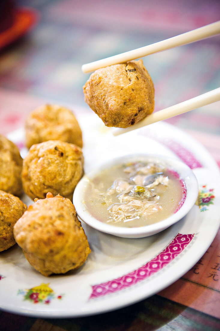 Fish balls beside bowl of dip on plate, chopsticks