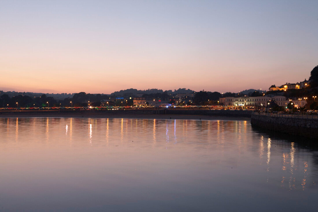 Blick übers Meer auf Küste von Torquay bei Nacht, beleuchtet.