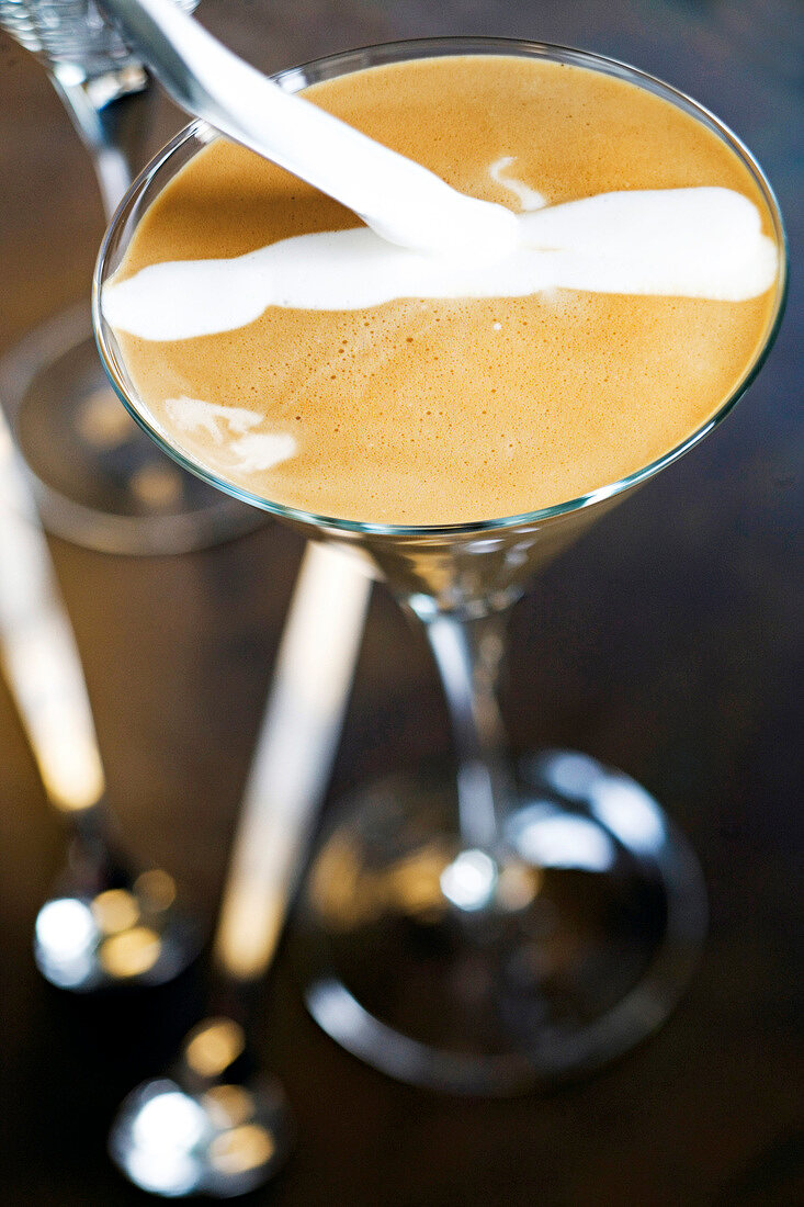 Cream being poured to espresso with spatula in cocktail glass, step 3