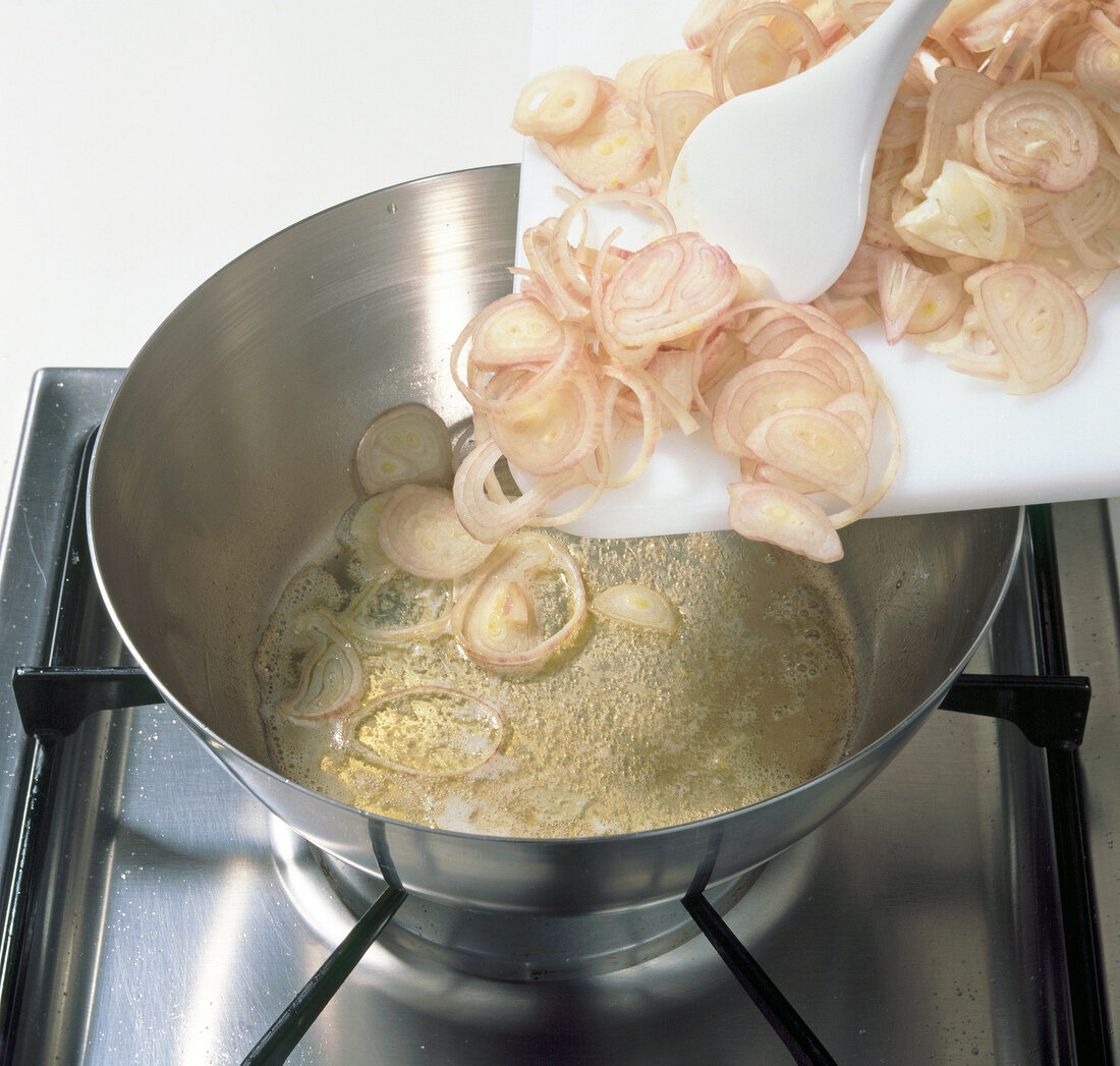 Chopped onions being put in pot with butter