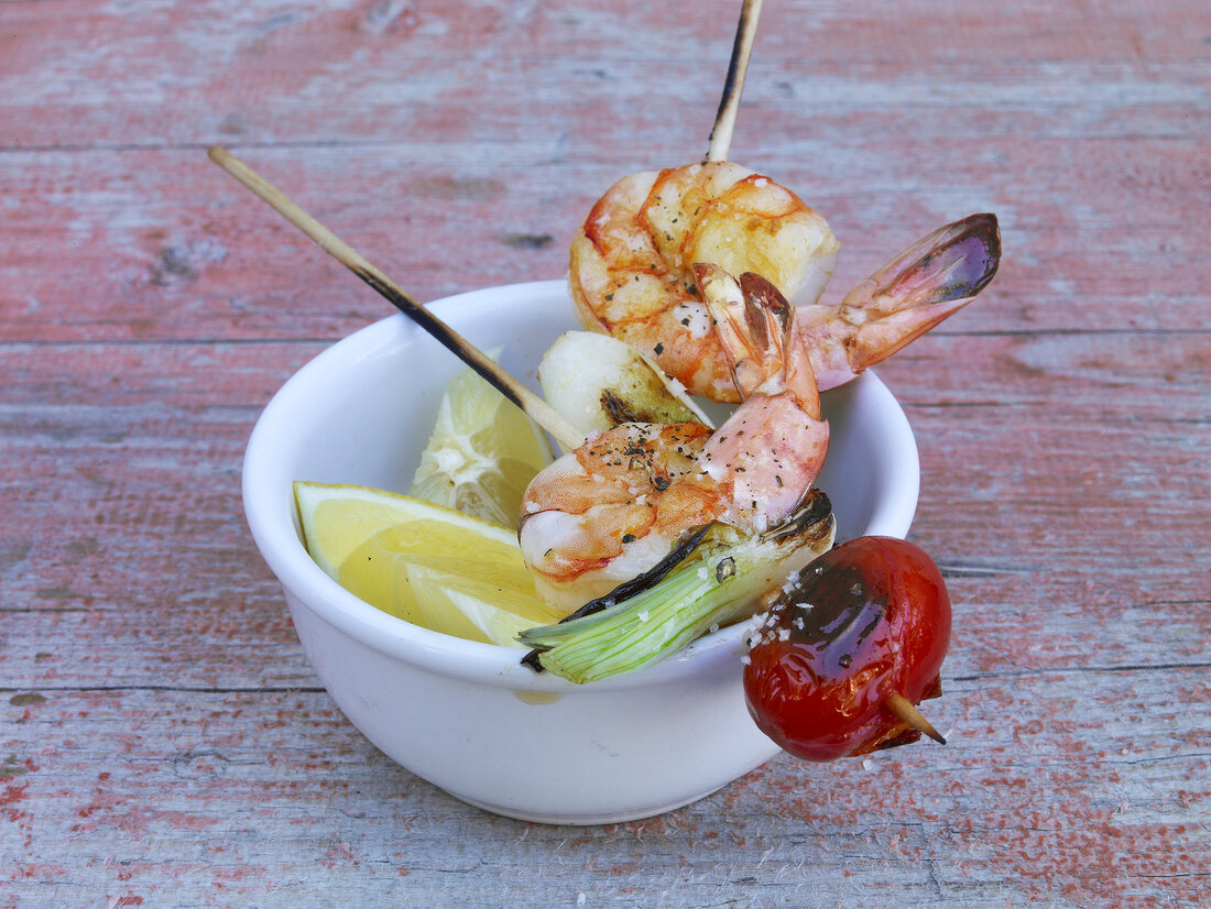 Bowl of shrimp skewers and slices of lime on wooden background