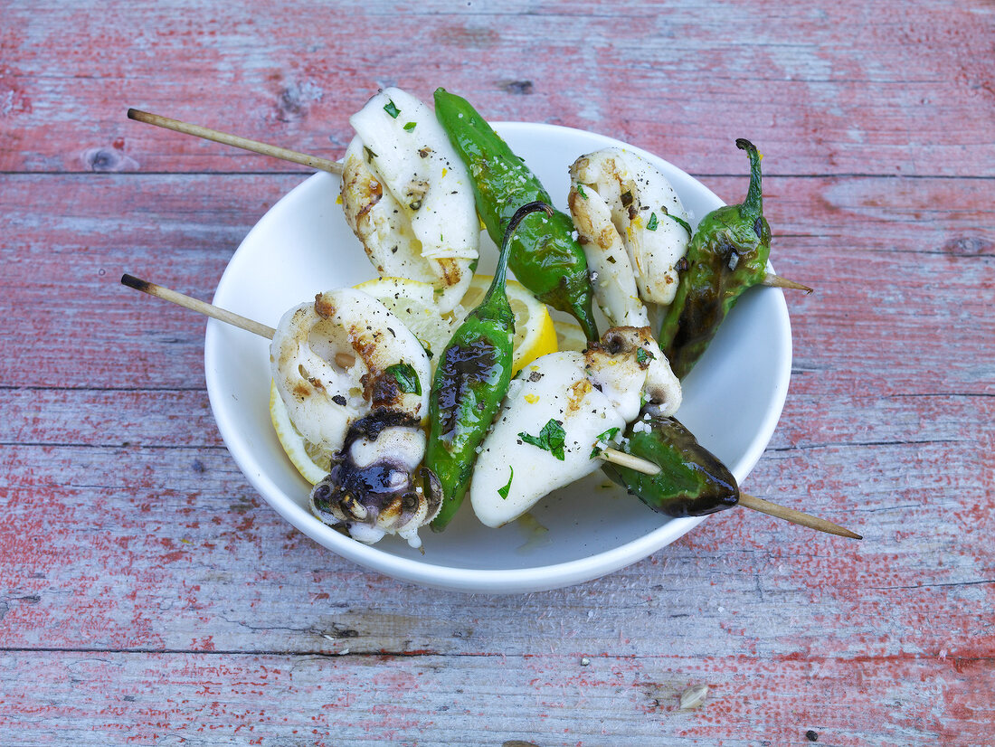 Bowl of mini squid skewers on wooden background