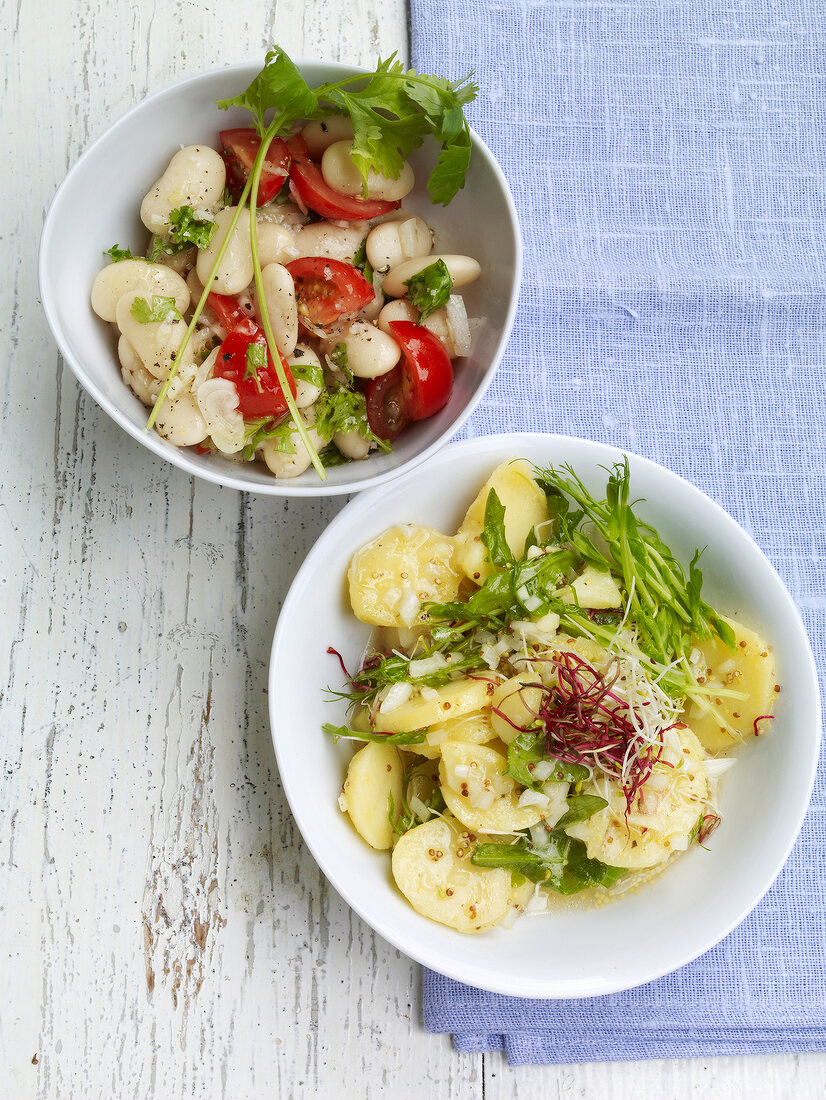 Two bowls of green beans and potato with tomato salad