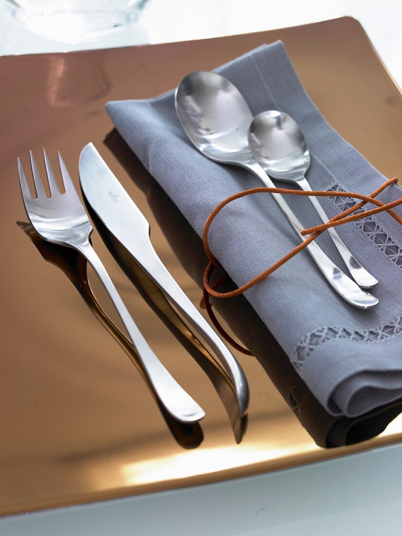 Silver cutlery and a blue napkin on a golden plate
