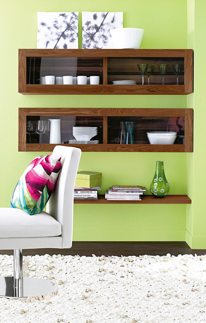 Green walls, wall shelves made of walnut wood and white chair with cushion in living room