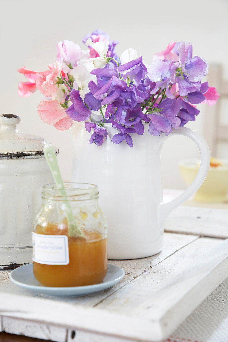 Colourful flowers in white milk jug with apple compote in glass jar on table