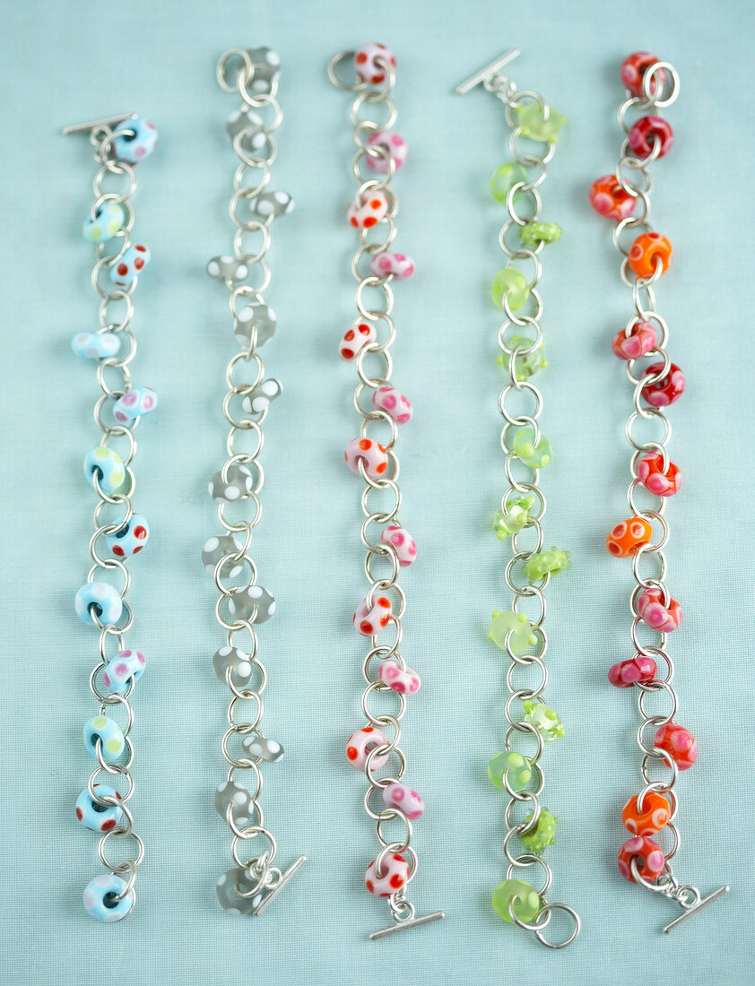 Close-up of five bracelets made of colourful glass rings and silver link chains