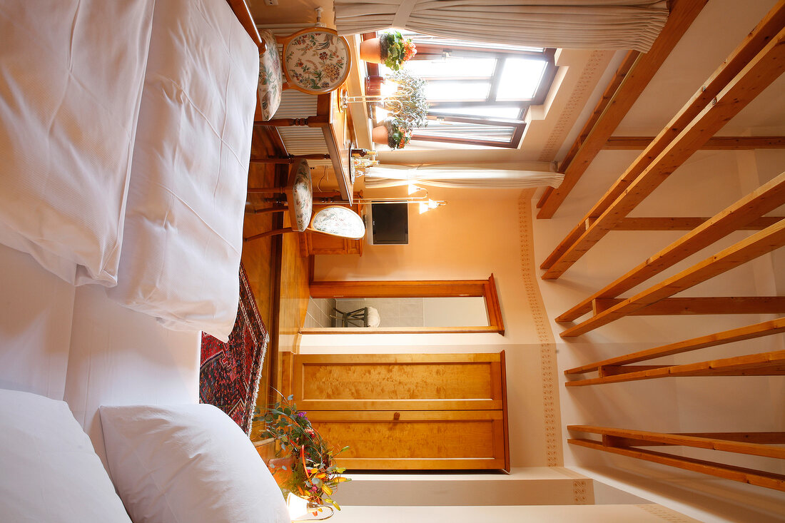 Interior of bedroom with wooden ceiling, bed, cushion, chair and table in hotel, Germany