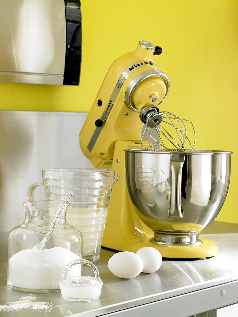 Yellow food processor with blender, mixing bowl, eggs, milk and flour on kitchen stand