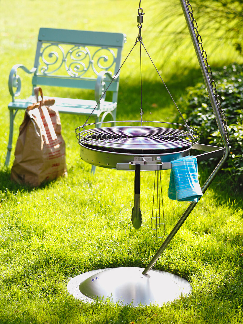 Stabiler Schwenkgrill aus Edelstahl im Garten, Sitzbank, Grillkohle