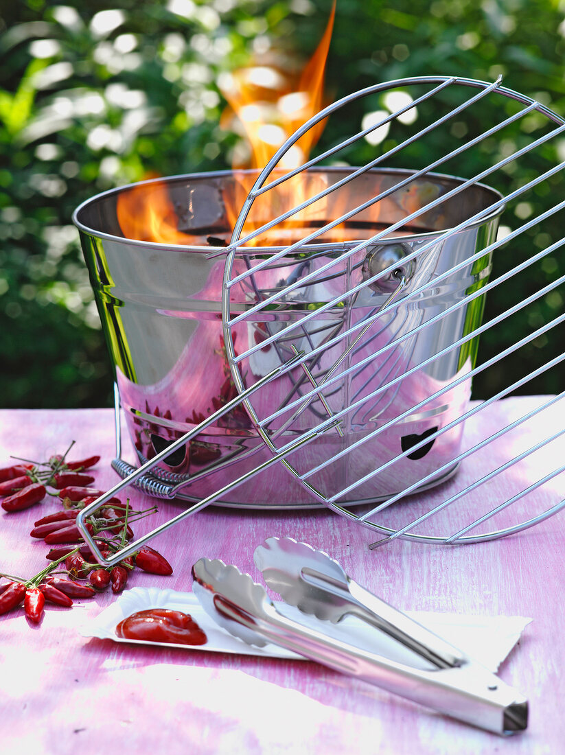 Stainless steel grill bucket with tongs and red chilies